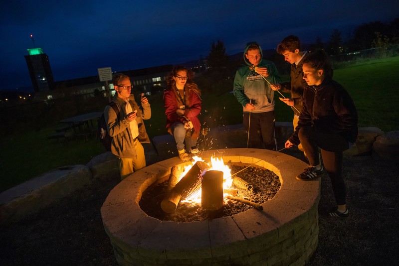 Five students enjoying s'mores over the Mountainview fire pit in 2018