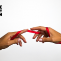 A close up of the hands of a female person of color holding a red ribbon.