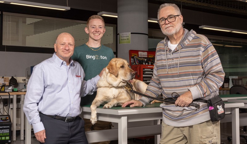 From left, Tom D’Onofrio, director of quality for BAE Systems’ power and propulsion solutions business area in Endicott, N.Y.; Eric Matson ’22; and service dog Colonel Dave with veteran John Coulton. BAE sponsored a project through America's VetDogs for a Watson College senior capstone team to build an alert device that would help Coulton.