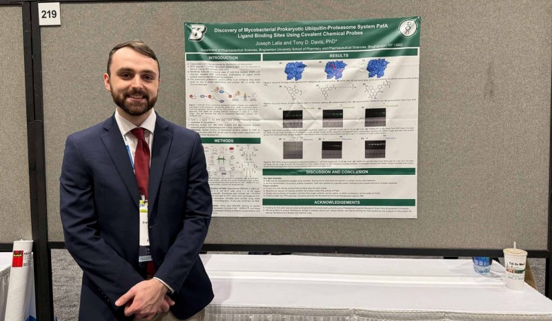 Fourth-year PharmD student Joseph Lalla standing alongside his capstone research poster at Midyear 2024.